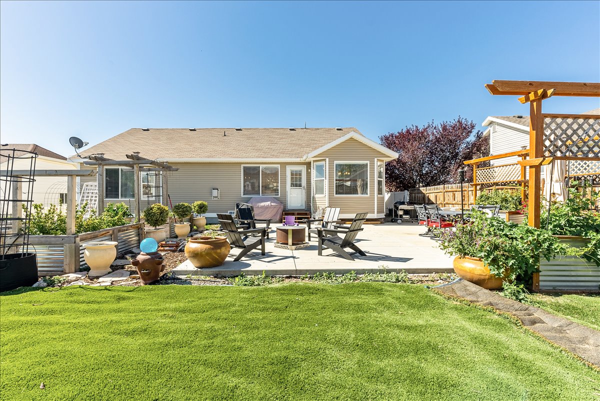 Expansive backyard featuring a concrete patio, artificial turf lawn, and multiple raised garden beds