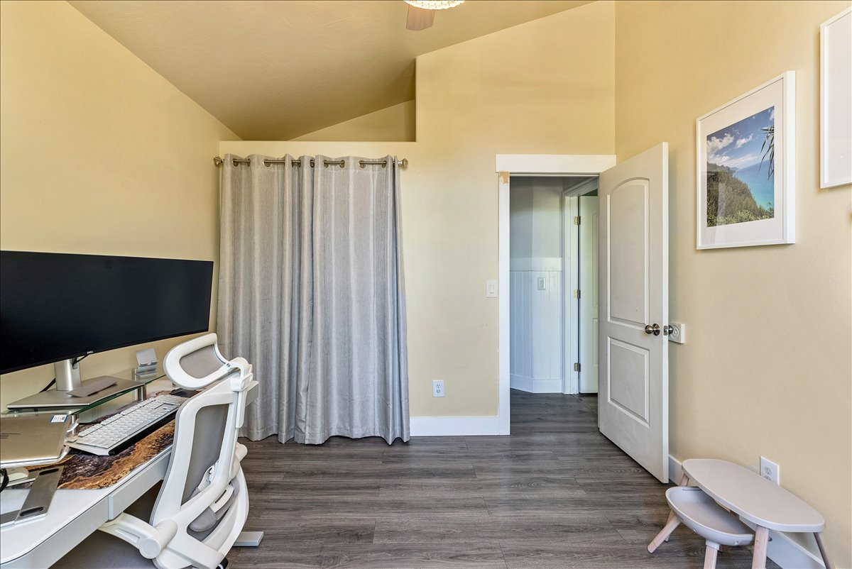 Vaulted ceilings define this space, featuring wood-finish flooring, a two-panel interior door, and crisp white baseboards and trim