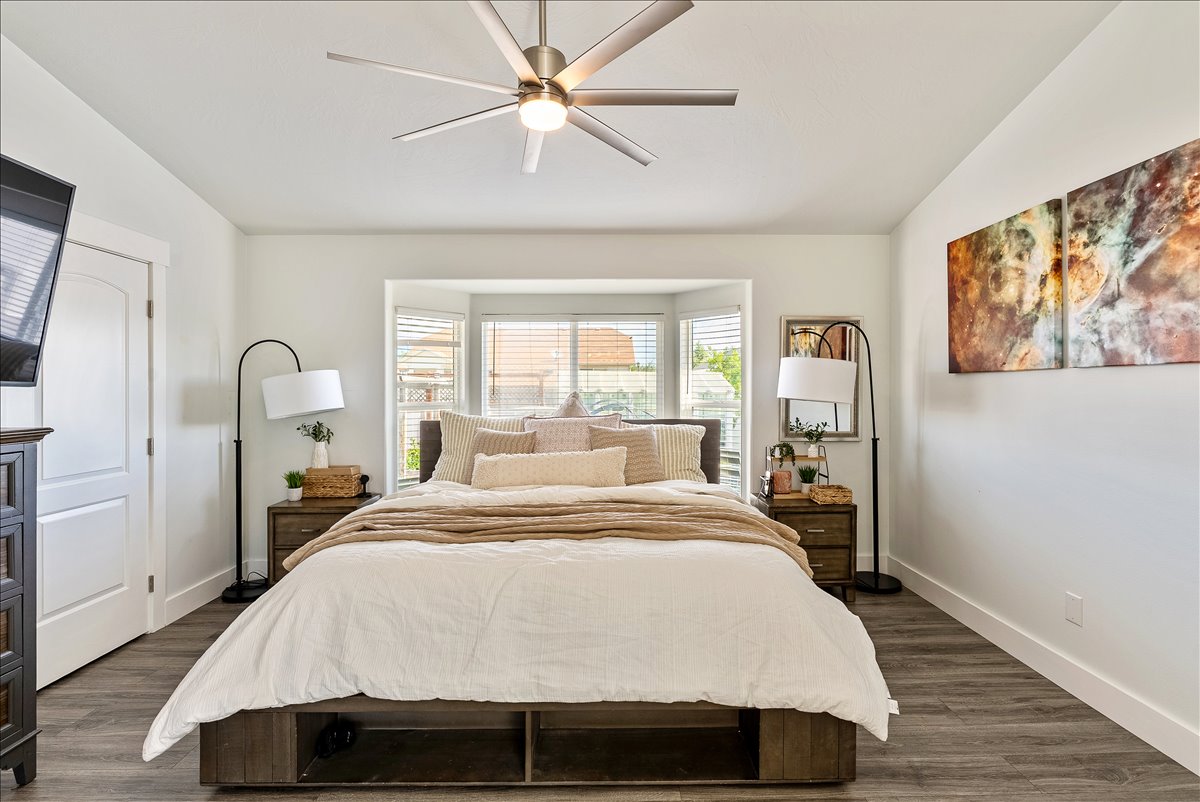 Spacious room featuring a bay window with blinds, wood-finish flooring, a contemporary ceiling fan, and white baseboards