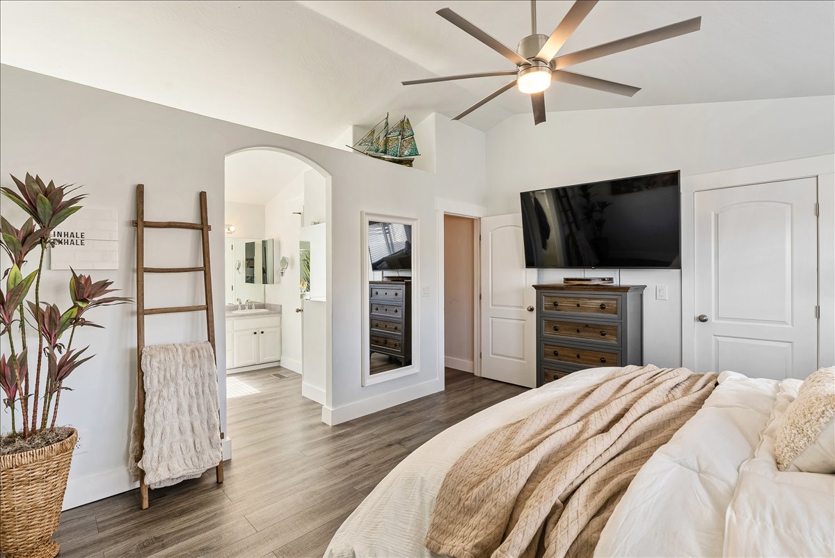Spacious bedroom featuring vaulted ceilings, wood-finish flooring, an arched doorway, and an attached full bathroom with a dual vanity