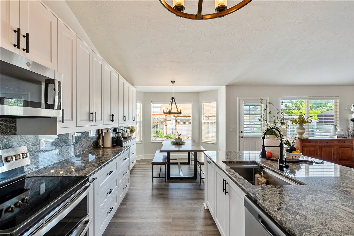 Contemporary kitchen featuring white cabinetry, dark hardware, stainless steel appliances, and wood-finish flooring