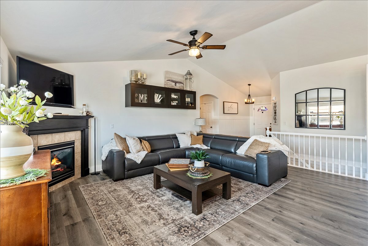 Spacious living area featuring vaulted ceilings, wood-finish flooring, and a fireplace with a tile surround and dark wood mantel