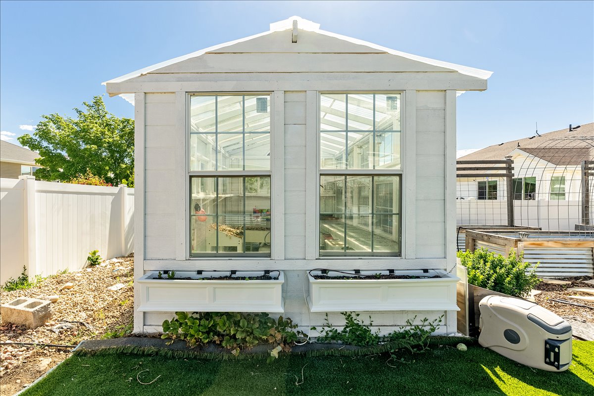 Greenhouse structure featuring a white exterior, large multi-pane windows, a peaked roofline, and two window boxes