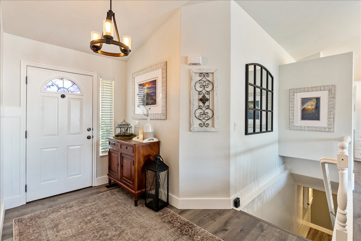 Entryway featuring a white door with an arched stained-glass insert, wood-finish flooring, white wainscoting, and a multi-light chandelier