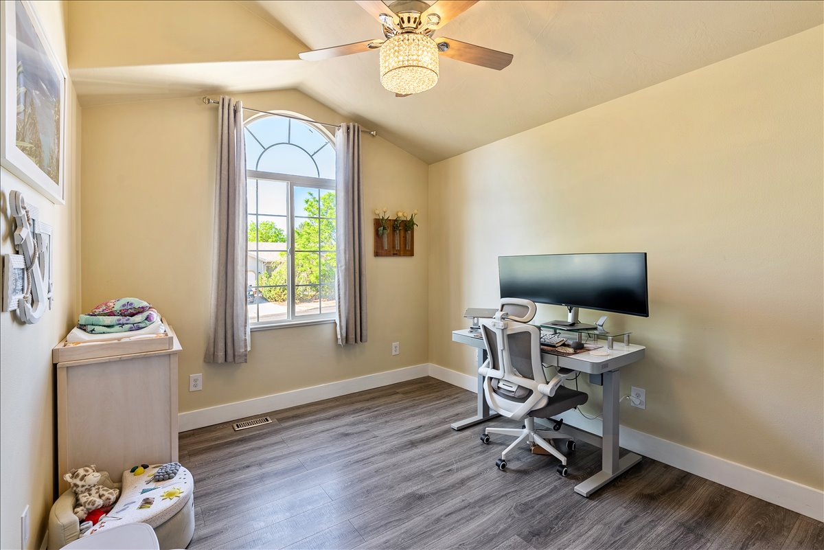 Vaulted ceiling room featuring an arched top window, wood-finish flooring, a ceiling fan with integrated lighting, and neutral wall tones