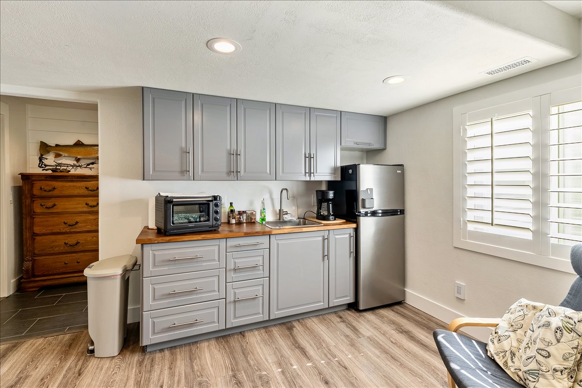 Kitchenette featuring wood-finish flooring, shaker-style cabinetry, a stainless steel refrigerator, a built-in sink, and plantation shutters