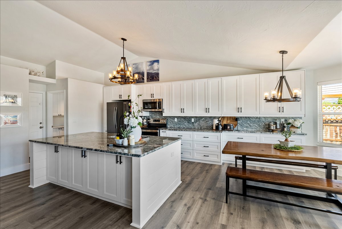 Kitchen featuring an expansive island with stone countertop, white shaker cabinetry, dark hardware, and wood-finish flooring