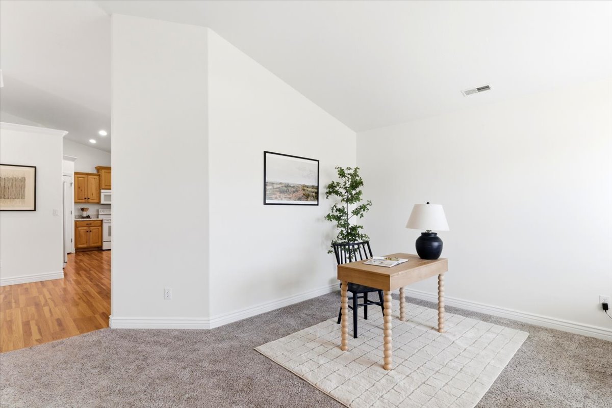 Carpeted room with white walls, baseboards, and a partial view of a kitchen with wood cabinetry and wood-finish flooring