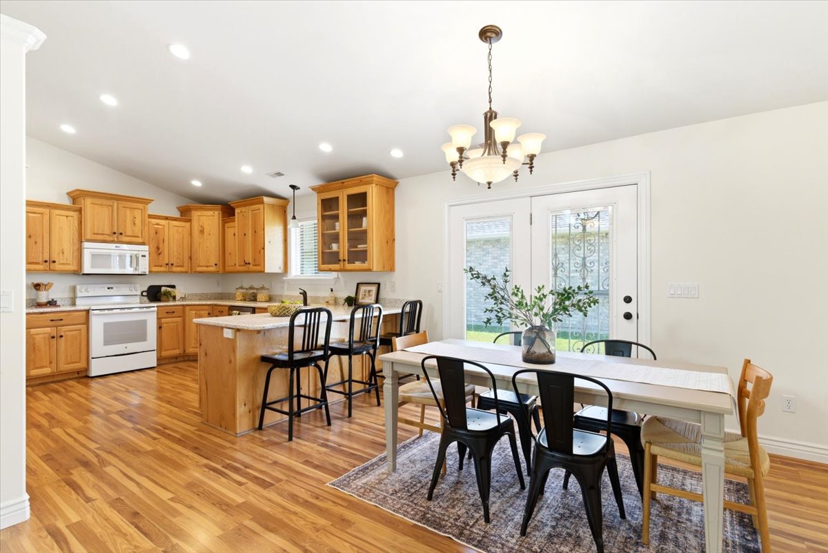 Spacious kitchen and dining area featuring wood-finish flooring, light wood cabinetry, white appliances, and a central island