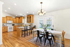 Spacious kitchen and dining area featuring wood-finish flooring, light wood cabinetry, white appliances, and a central island