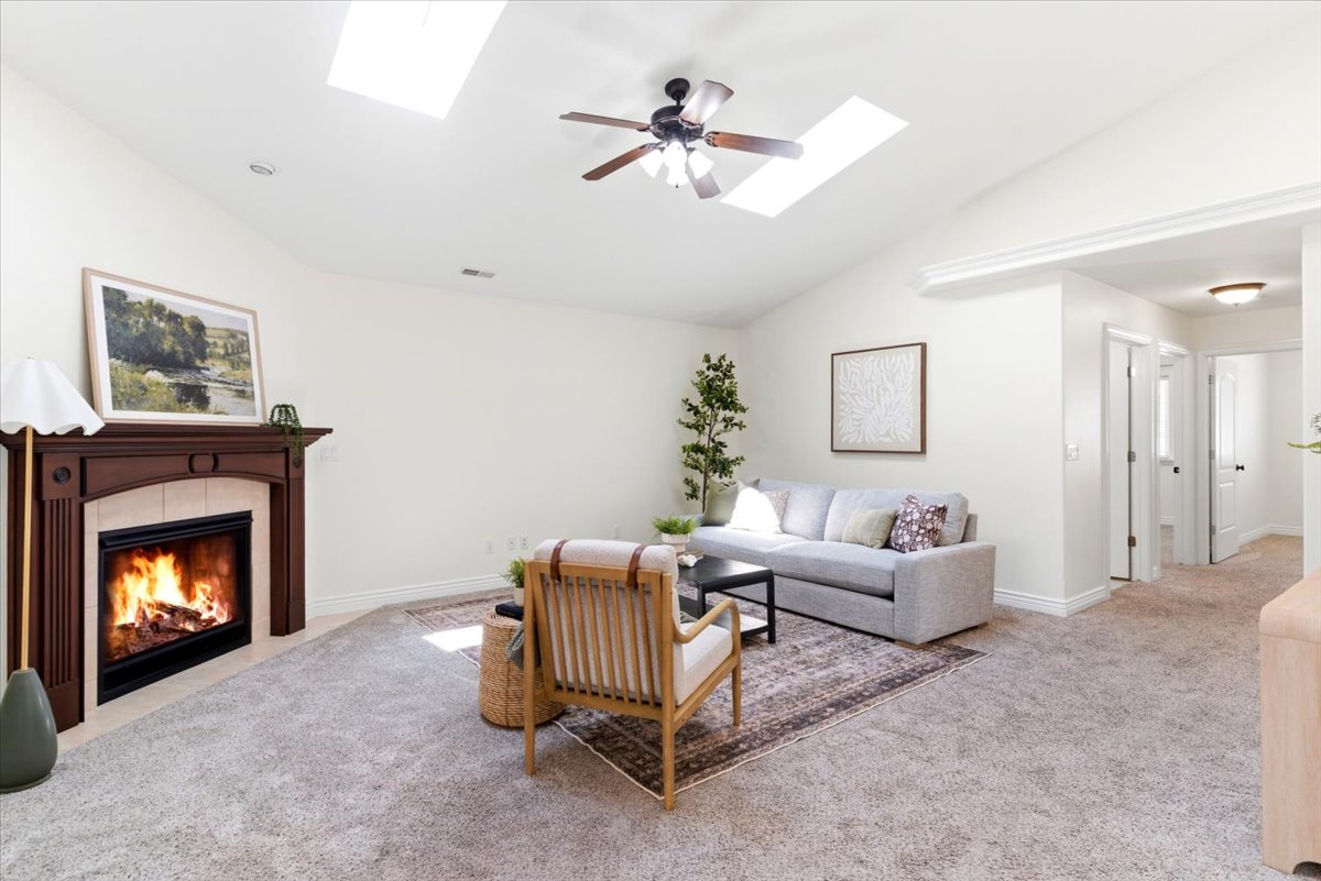 Living area featuring a fireplace with a wood mantle and tile surround, vaulted ceilings, two skylights, and a ceiling fan