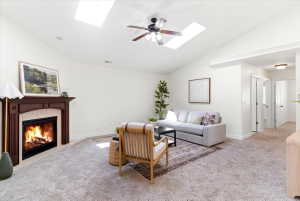 Living area featuring a fireplace with a wood mantle and tile surround, vaulted ceilings, two skylights, and a ceiling fan