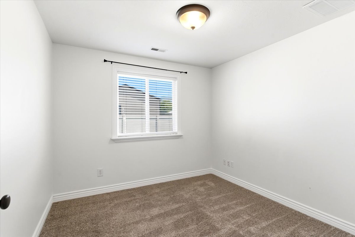 Carpeted room featuring a window with blinds, a ceiling-mounted light fixture, white walls, and white baseboards