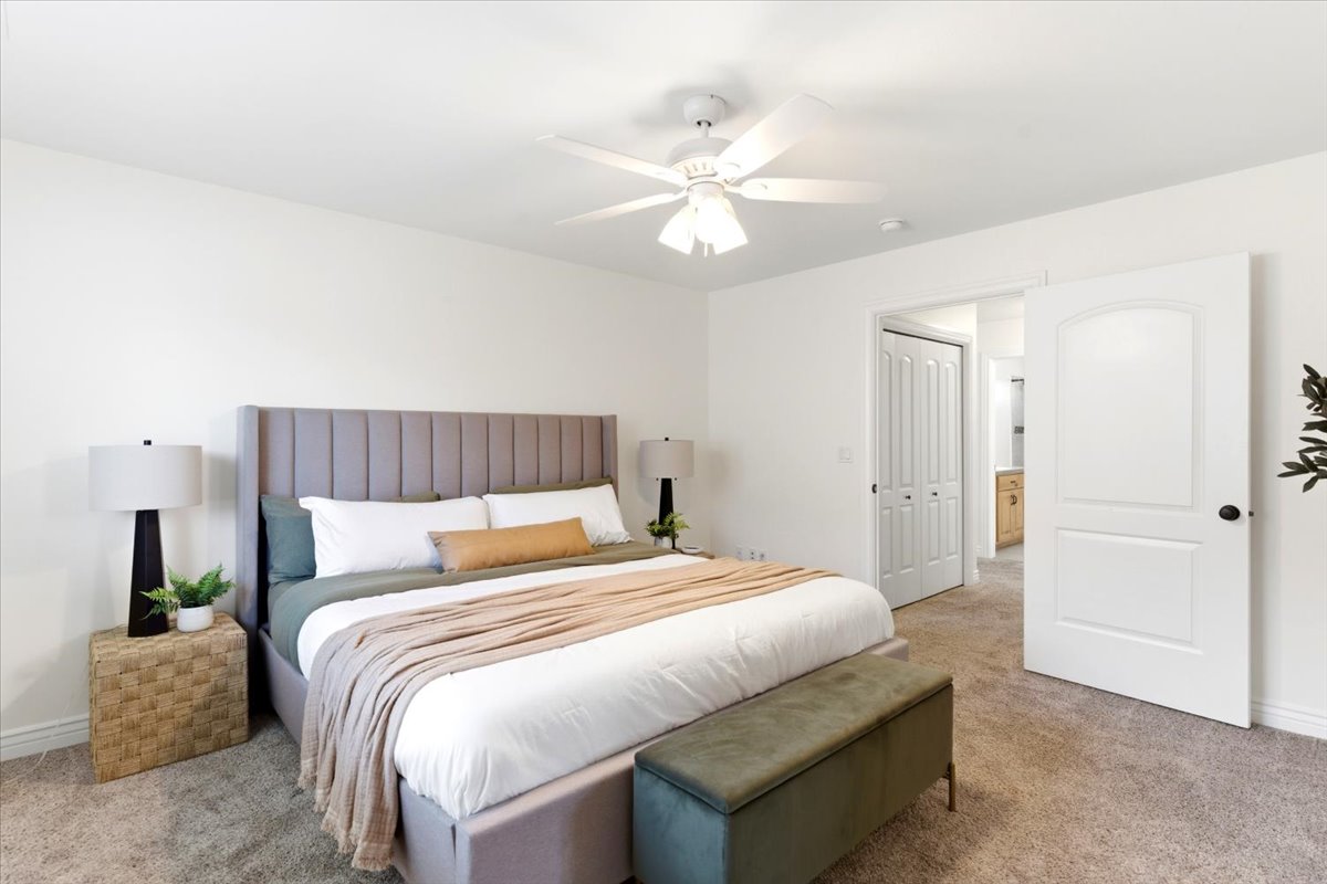 Spacious bedroom featuring plush carpeting, crisp white walls, and a contemporary ceiling fan