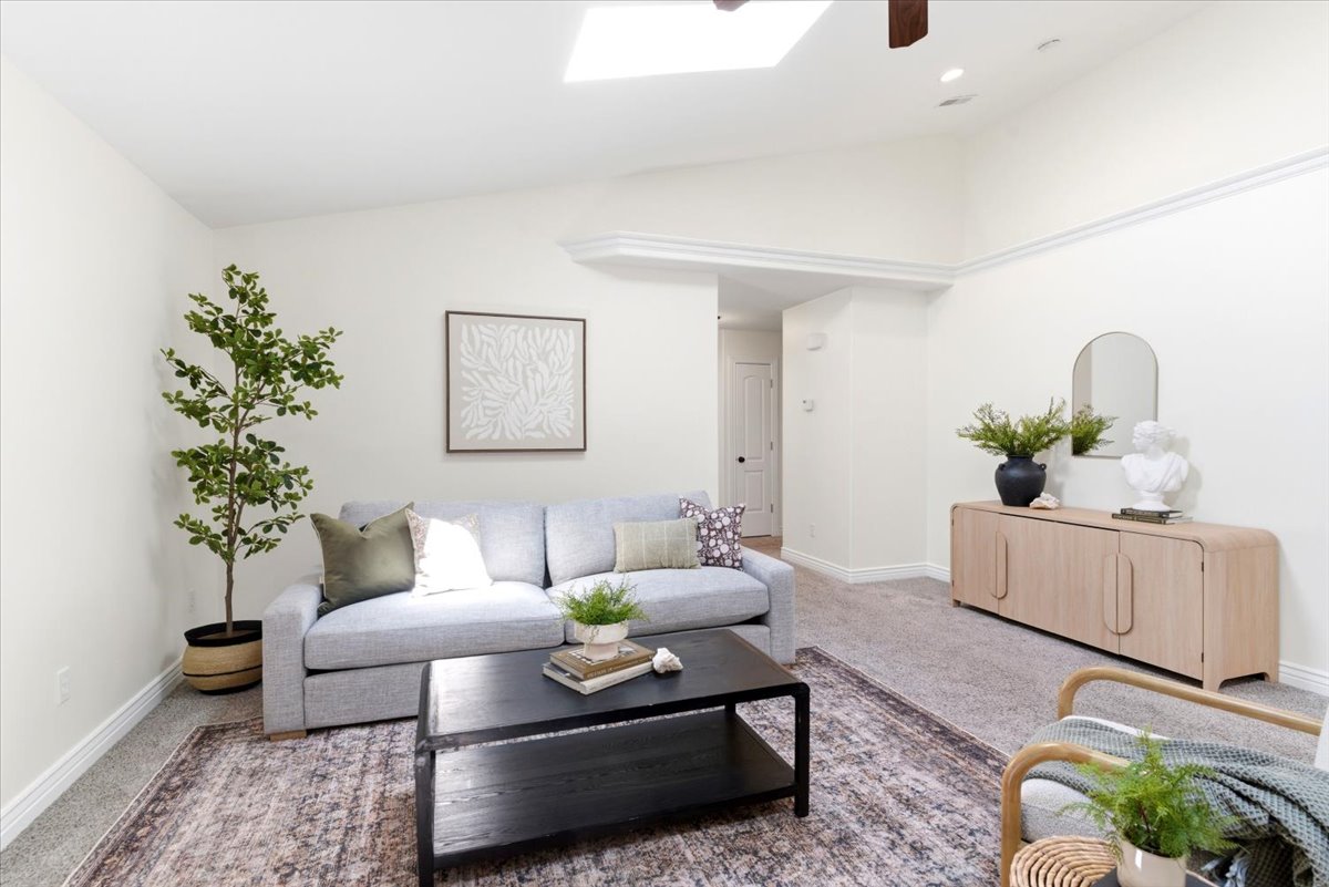 Living area featuring vaulted ceilings, a skylight, crown molding, light-toned carpeting, and white baseboards