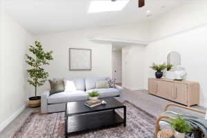 Living area featuring vaulted ceilings, a skylight, crown molding, light-toned carpeting, and white baseboards