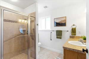 Glass-enclosed shower featuring neutral-toned tile work with mosaic accent banding, a window providing natural light, a wood-finish vanity with a speckled countertop and integrated sink, and tile flooring