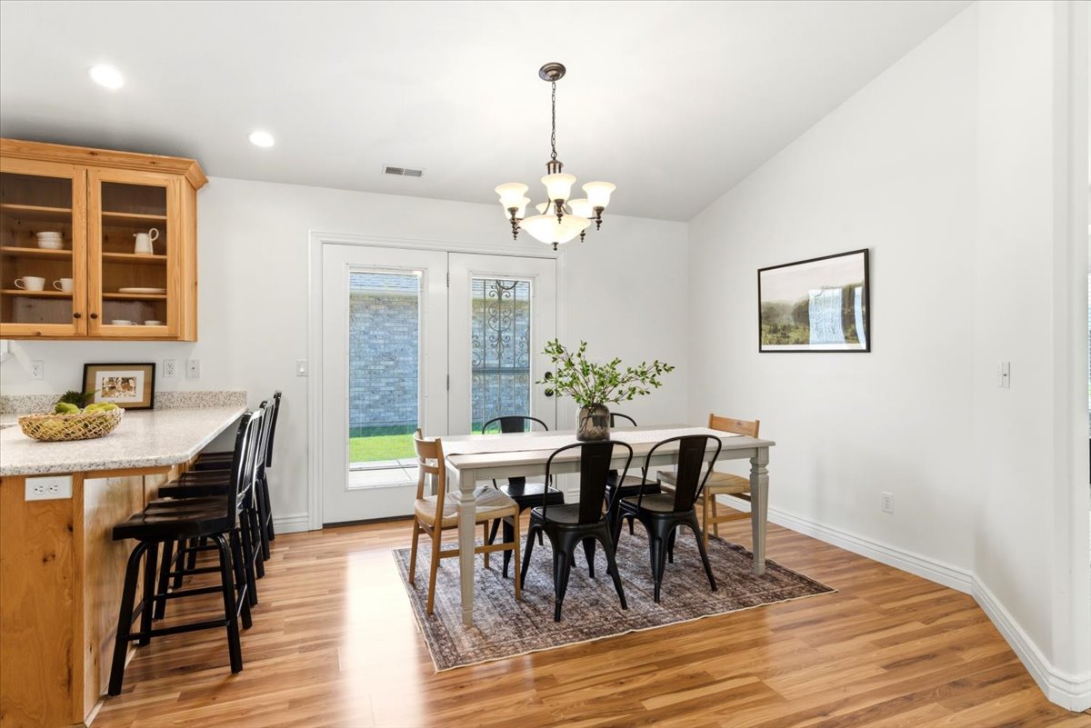Open-concept dining area with wood-finish flooring, a vaulted ceiling, and a traditional chandelier