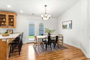 Open-concept dining area with wood-finish flooring, a vaulted ceiling, and a traditional chandelier