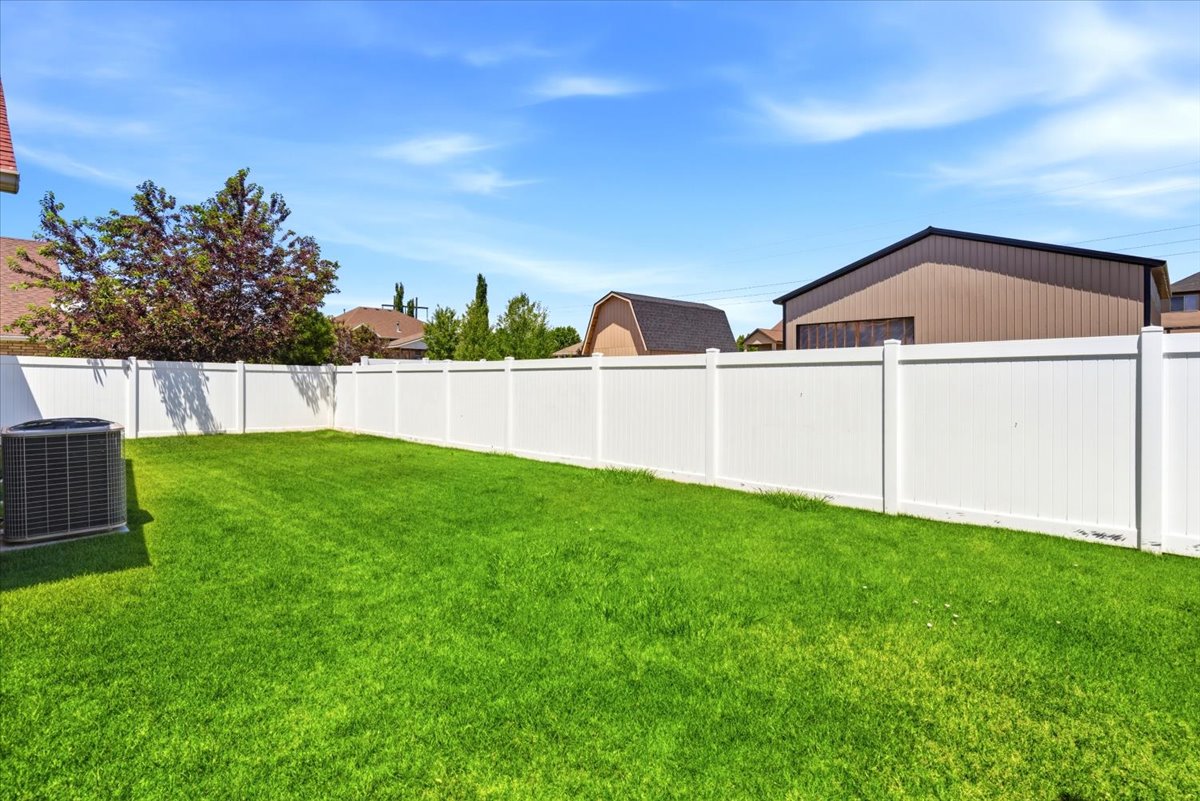 Generous rear yard featuring a manicured lawn, full privacy fencing, and an external air conditioning unit