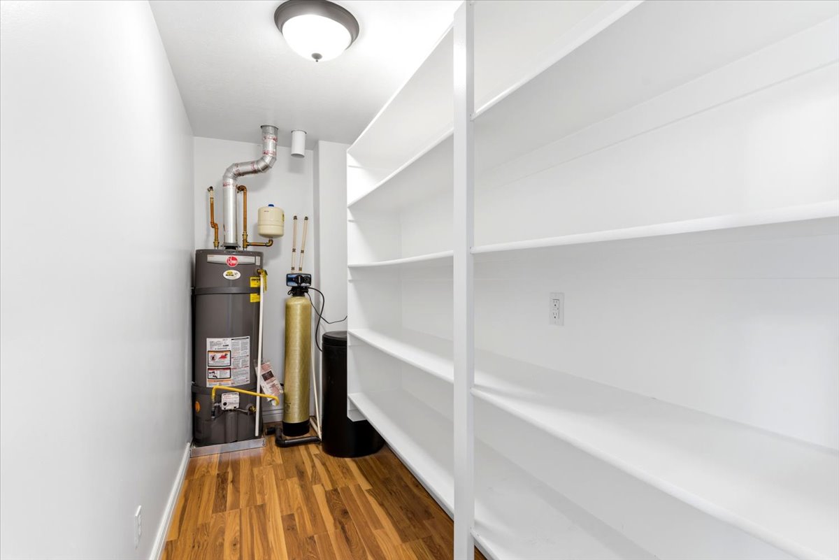 Utility space featuring wood-finish flooring, a water heater, a water softener, and built-in shelving