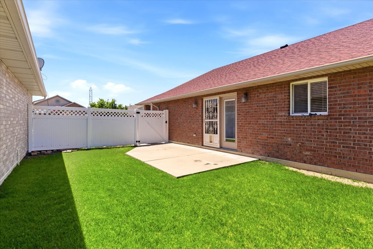 Backyard featuring a concrete patio, green lawn, white privacy fence with lattice accents, and brick exterior