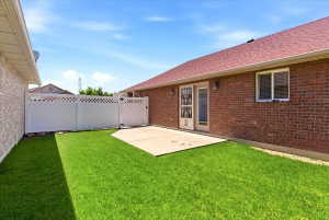 Backyard featuring a concrete patio, green lawn, white privacy fence with lattice accents, and brick exterior