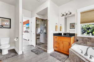 Spacious bathroom featuring a glass-enclosed shower, a separate soaking tub with tiled surround, a wood vanity with a dark countertop, and wood-finish flooring