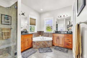 Spacious bathroom featuring a glass-enclosed shower, corner soaking tub, and dual wood-finish vanities with dark countertops