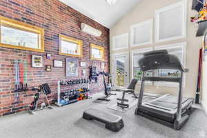 Vaulted ceiling room featuring a brick accent wall, abundant natural light from large windows, and direct outdoor access