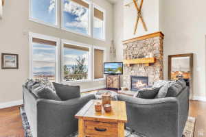 Great room featuring a floor-to-ceiling stone fireplace with a wood mantle, high ceilings, expansive windows with transoms, and wood-finish flooring