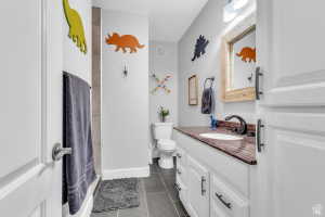 Bathroom featuring a vanity with a reddish-brown countertop, dark bronze-finish fixtures, a white undermount sink, and white cabinetry with dark bronze-finish hardware