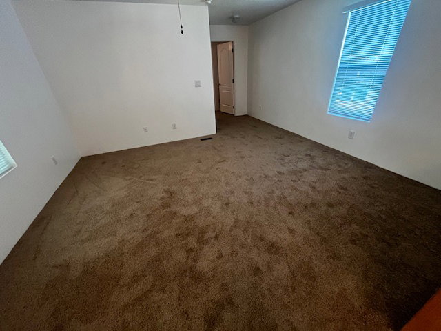 Spacious room featuring neutral wall paint, brown carpet flooring, and a ceiling fan