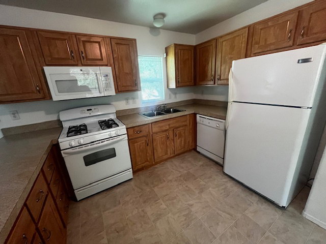 Kitchen featuring wood cabinetry, laminate countertops, a gas range with an overhead microwave, a white refrigerator, and tile-finish flooring