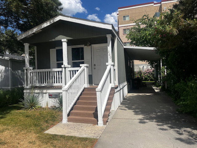 Exterior featuring a covered front porch with white railings, brown-toned steps, and a carport