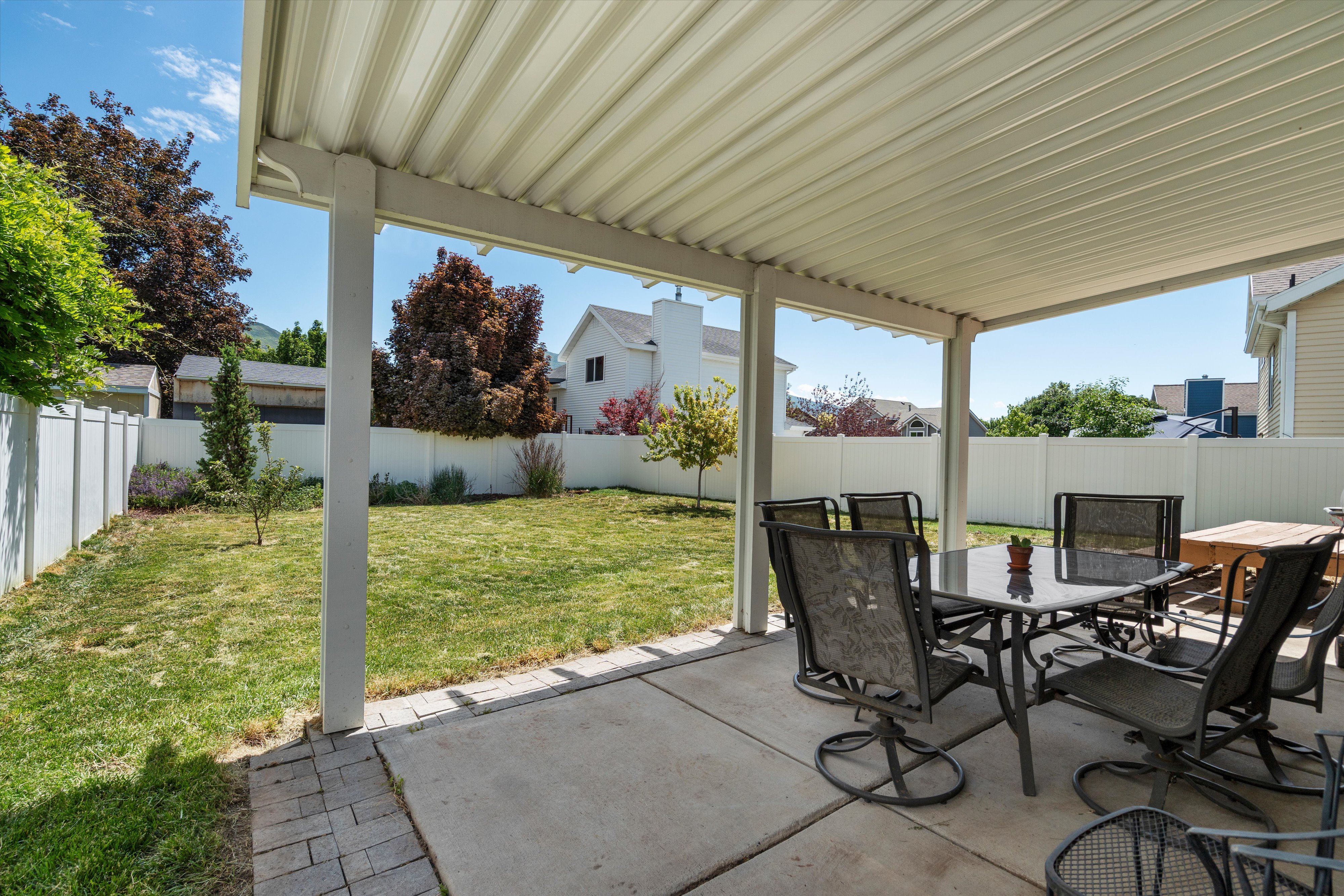 Covered patio with concrete flooring, supported by white posts, and bordered by a paver edge