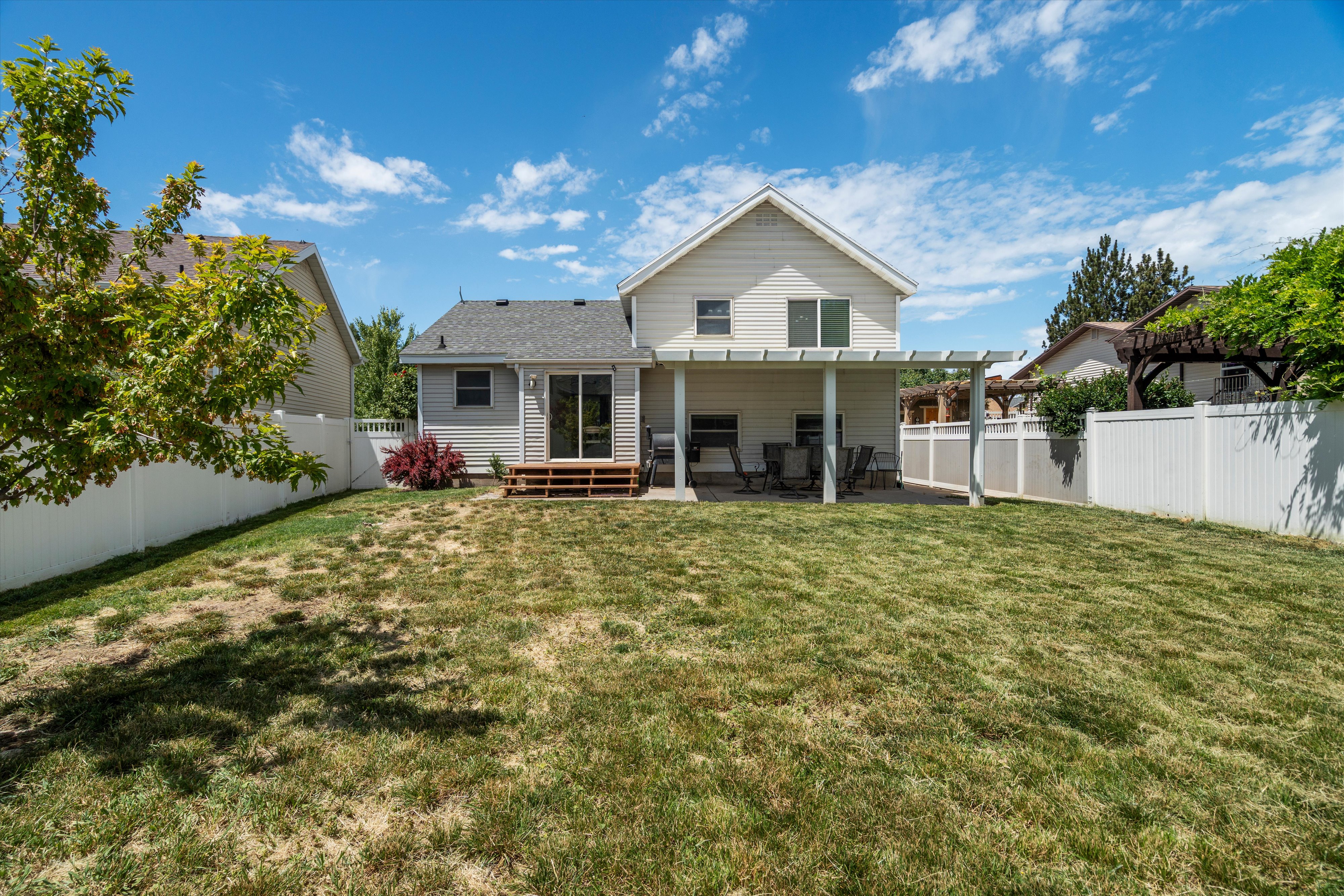 Spacious backyard featuring a substantial lawn area, a white privacy fence, and a multi-level deck with a pergola