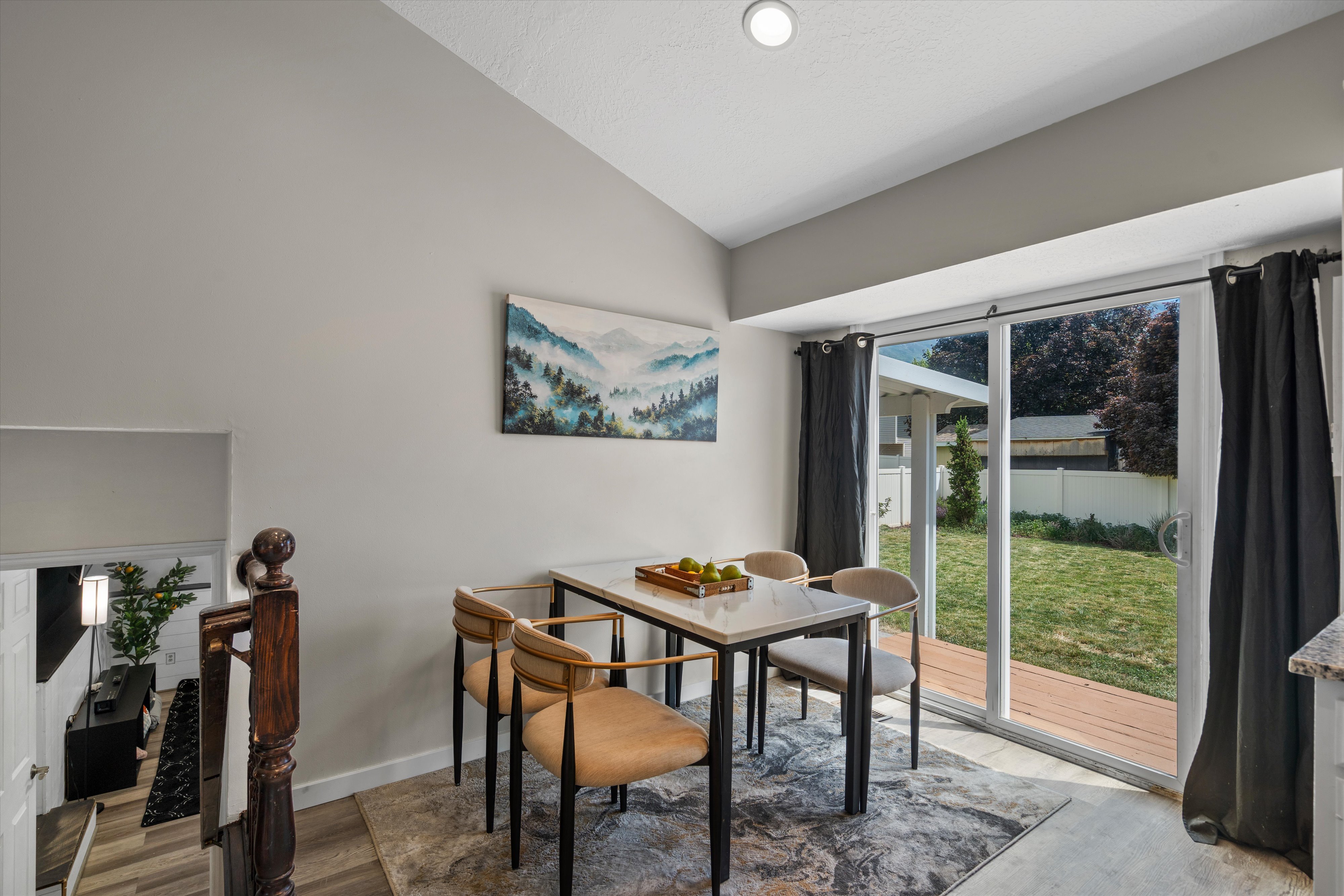 Vaulted ceiling dining area with recessed lighting, featuring wood-finish flooring, a sliding glass door to an exterior wood-decked patio, and a wooden banister