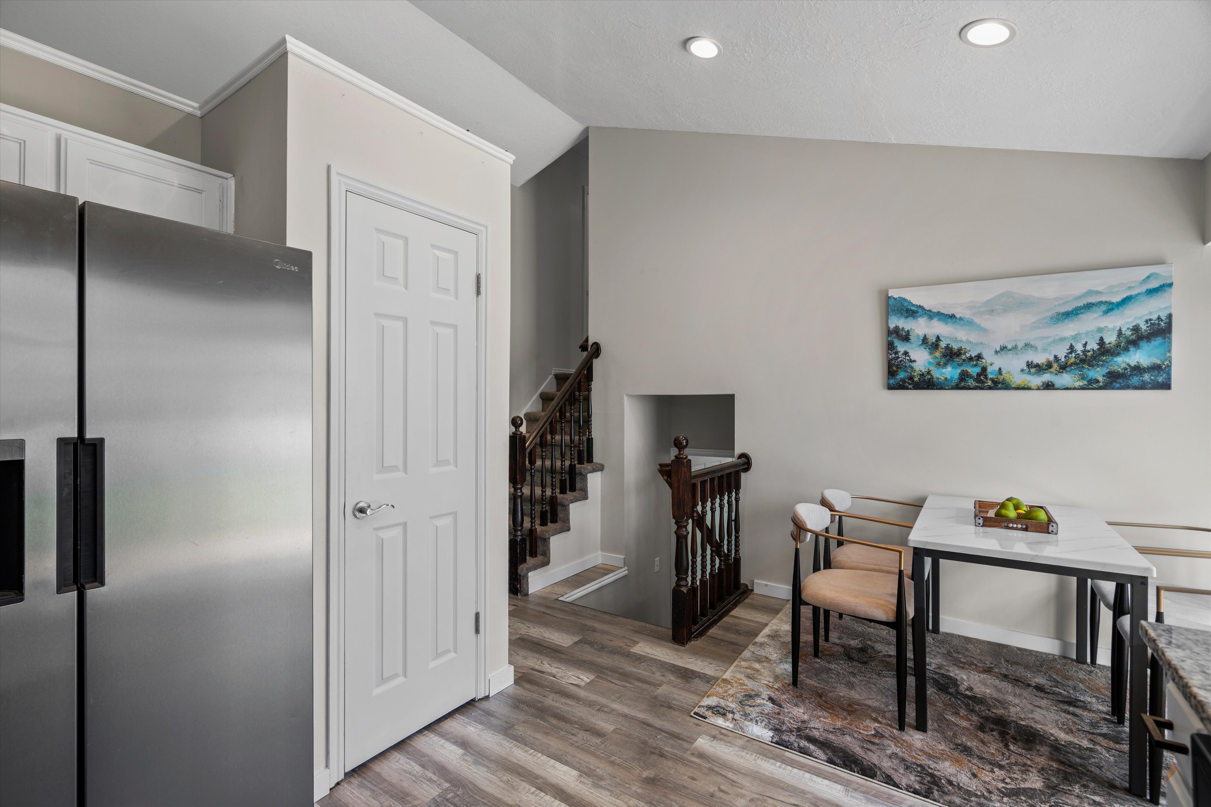Kitchen area featuring stainless steel refrigerator, white paneled doors, wood-finish flooring, recessed lighting, and a dark wood staircase with balusters