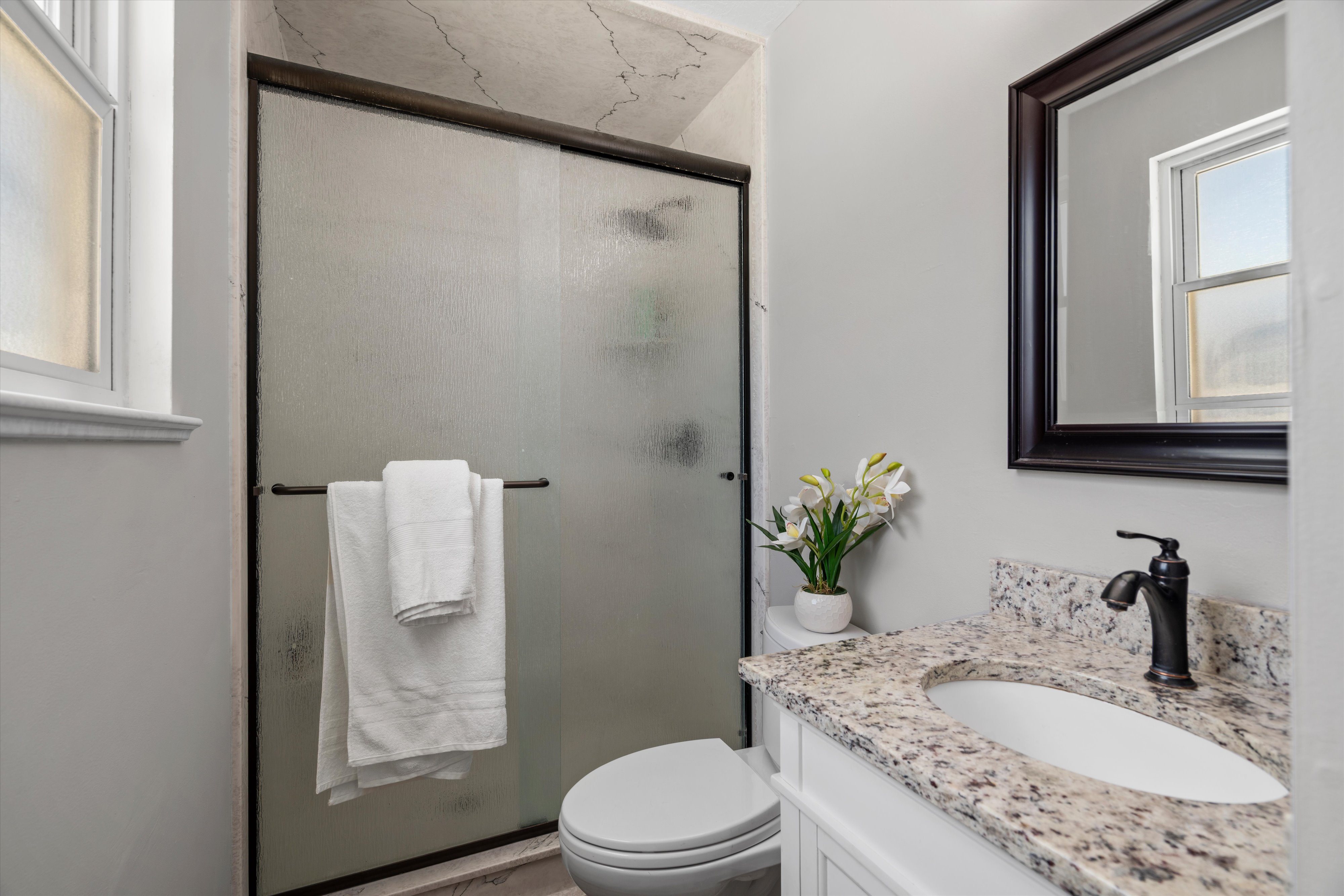 Full bathroom featuring a frosted glass shower enclosure, white vanity with a granite-style countertop, undermount sink, and oil-rubbed bronze faucet