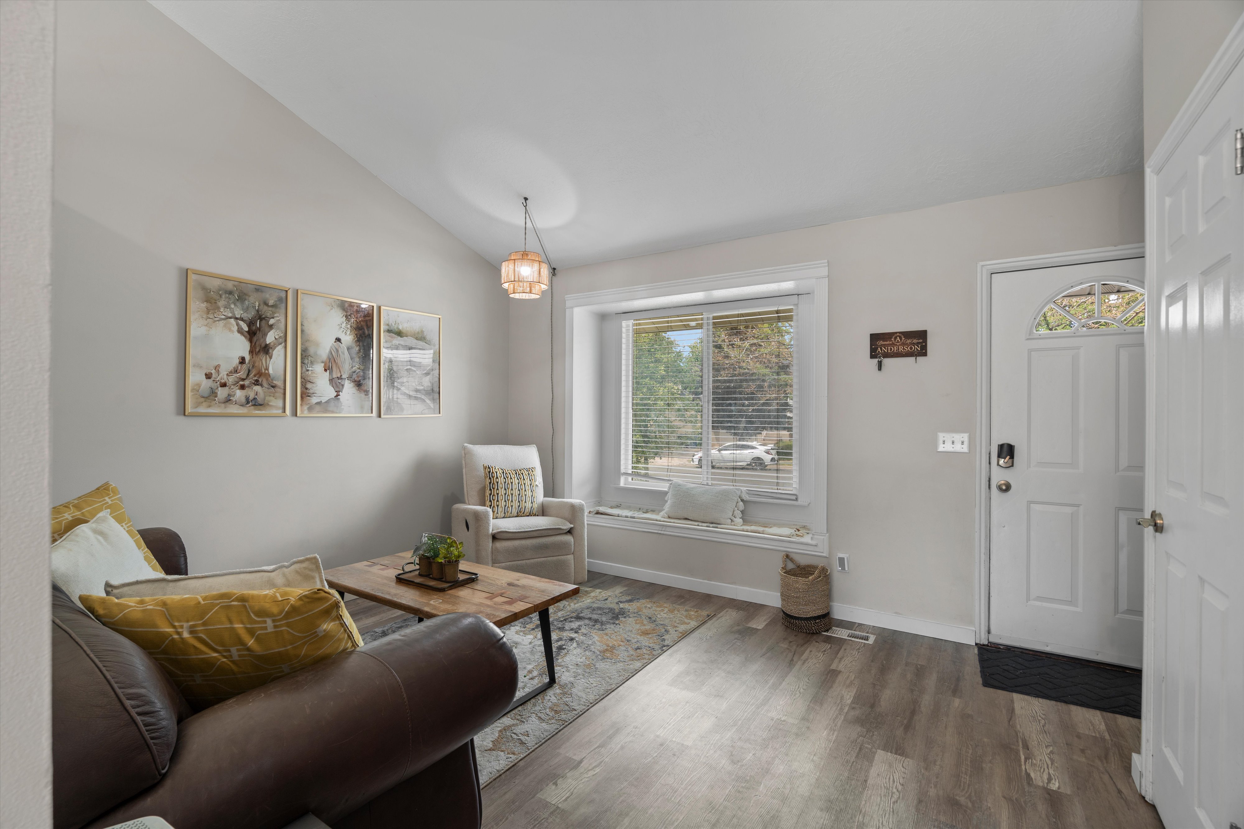Living area featuring vaulted ceilings, wood-finish flooring, a contemporary pendant light fixture, a window seat with a built-in shelf, and a white front door with an arched glass insert