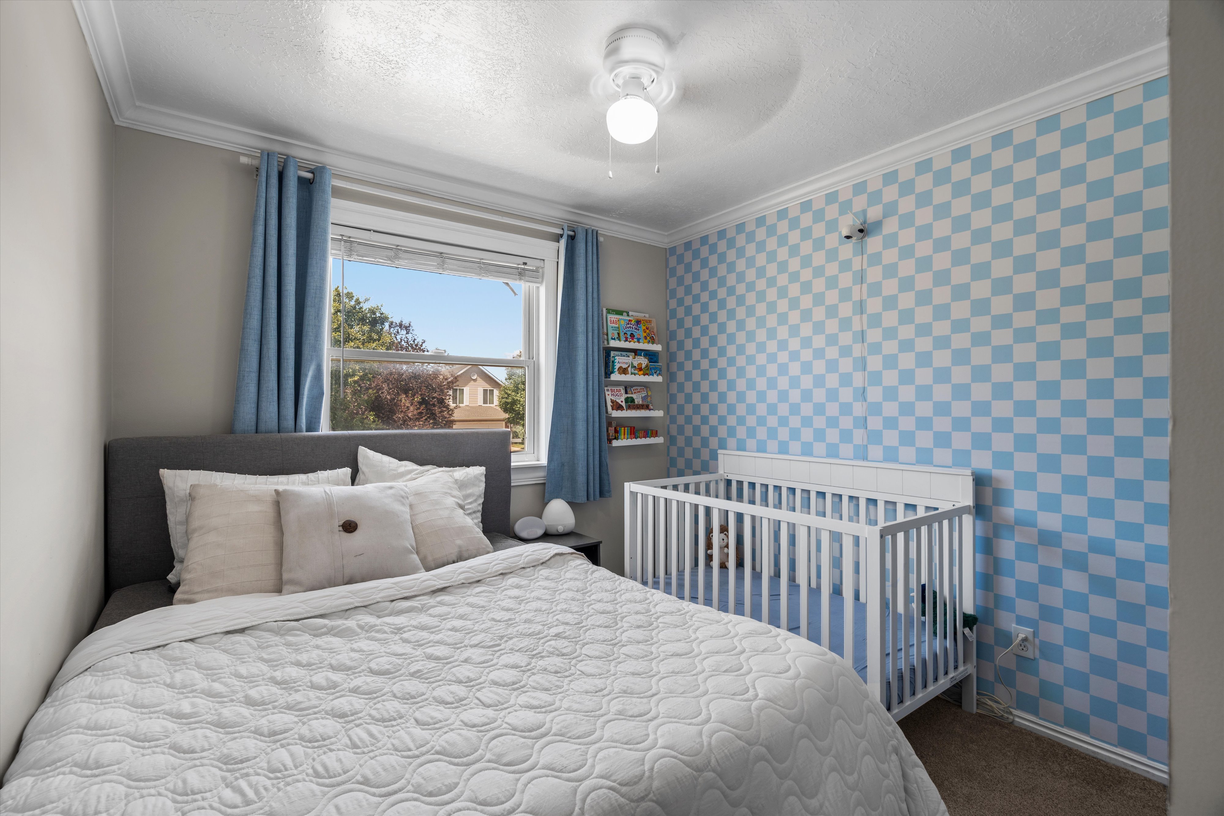 Bedroom featuring checkerboard accent wall, window with blinds, ceiling fan with light fixture, and crown molding