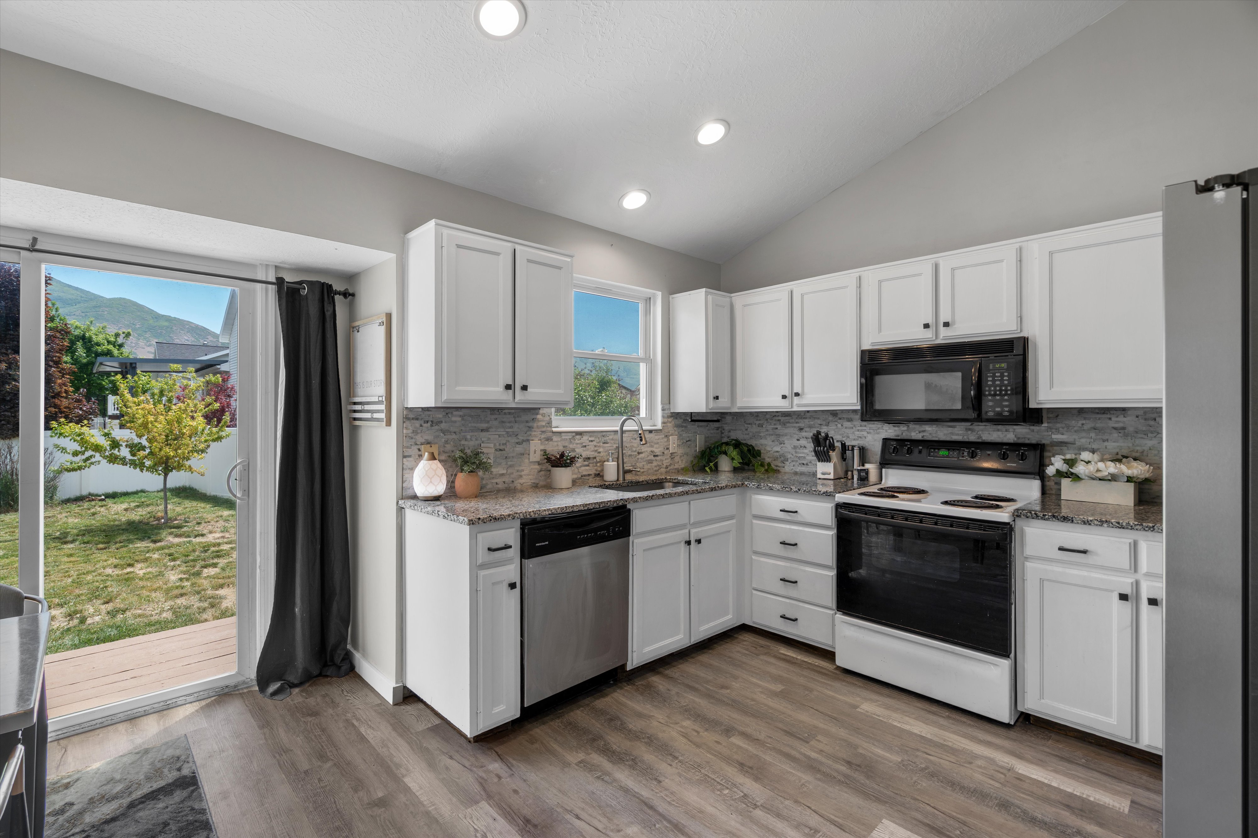 Kitchen featuring wood-finish flooring, white cabinetry, granite-style countertops, mosaic tile backsplash, and a sliding glass door to the exterior