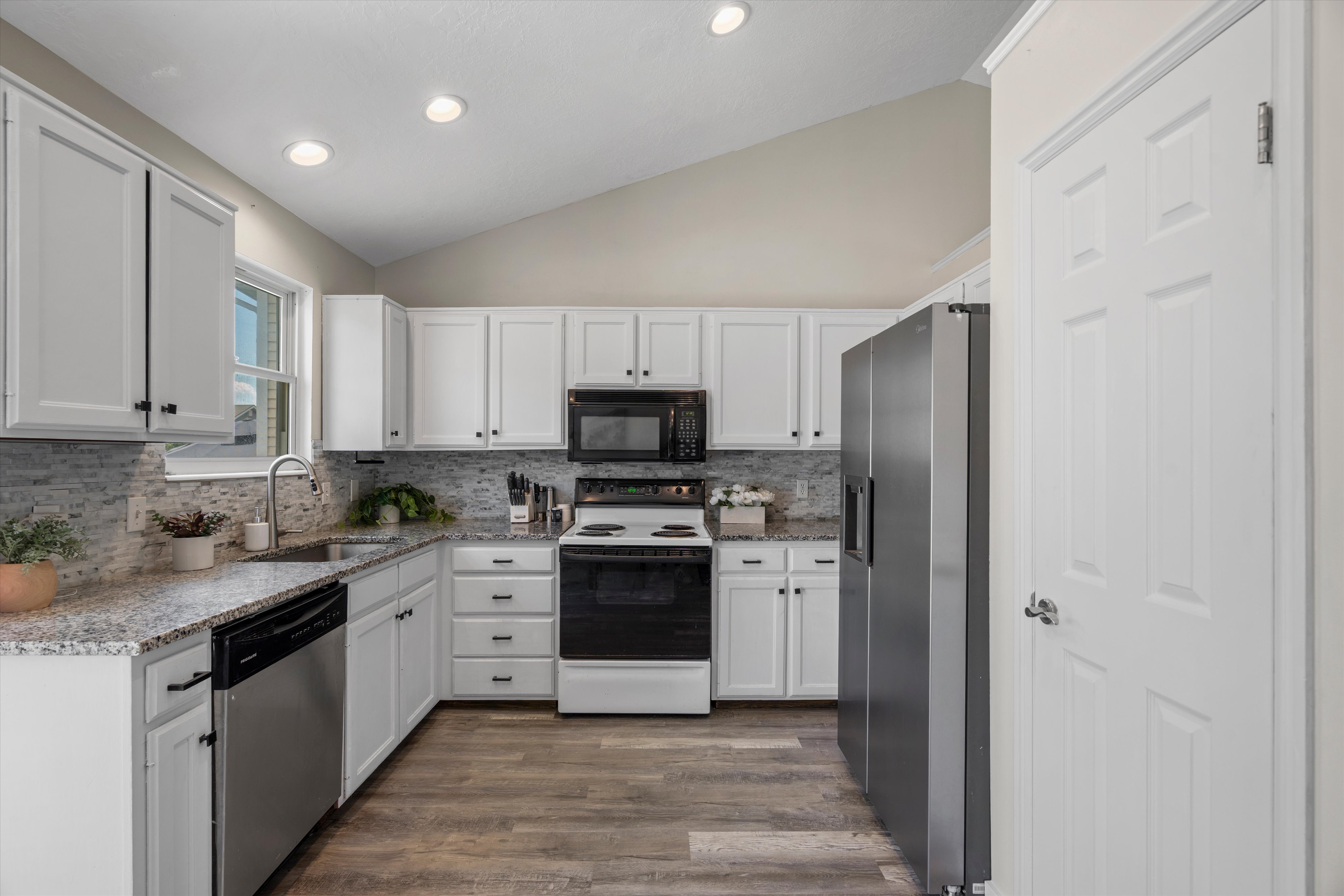 Kitchen featuring wood-finish flooring, white cabinetry with dark hardware, stone-look countertops, and a tile backsplash