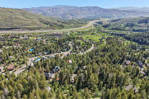 Expansive mountain landscape featuring a valley with residential properties, dense tree coverage, and distant highway infrastructure