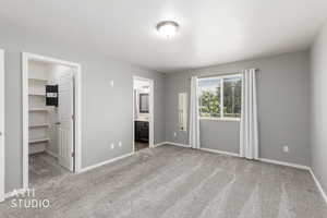 Carpeted room featuring a window with blinds, a ceiling-mounted light fixture, a walk-in closet with built-in shelving, and access to a full bathroom