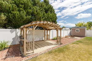 Wood pergola over a sand patio, featuring a fire pit area, a storage shed, and a white privacy fence