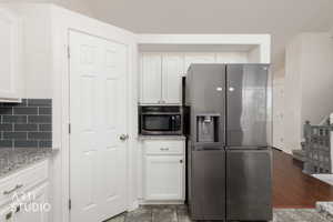 Kitchen featuring white shaker-style cabinetry with chrome hardware, granite-style countertops, dark gray subway tile backsplash, and a stainless steel refrigerator