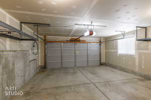 Spacious garage featuring a paneled overhead door, concrete flooring, overhead storage racks, and a window with blinds