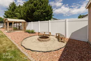 Backyard featuring a gazebo, fire pit area with two wooden benches, white privacy fencing, and decorative rock landscaping